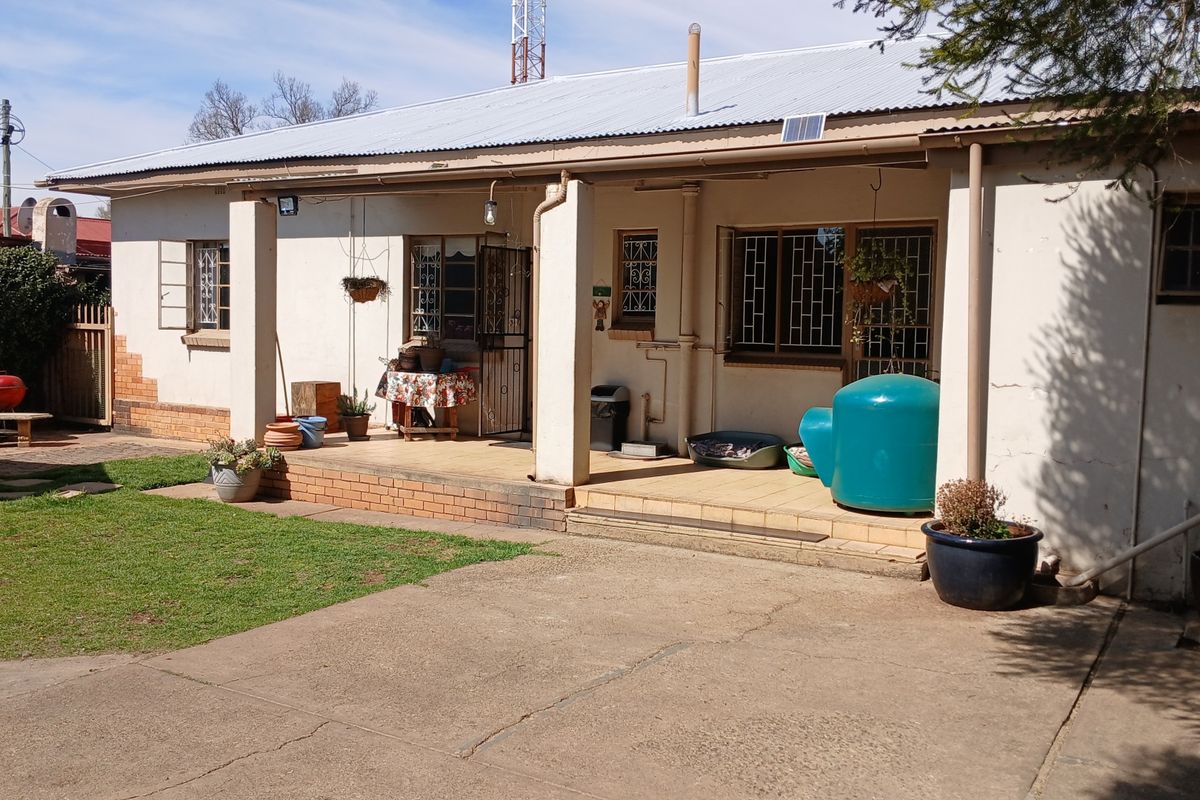 Rear view of the house featuring a covered patio with brick pillars, security gates, and a concrete driveway leading to the garden area.