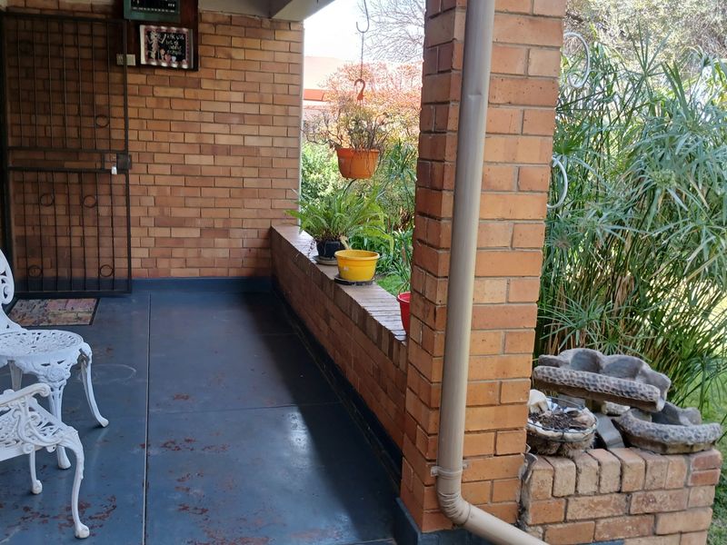 A covered patio area featuring exposed brick walls, a brick pillar, and a concrete floor overlooking the garden.