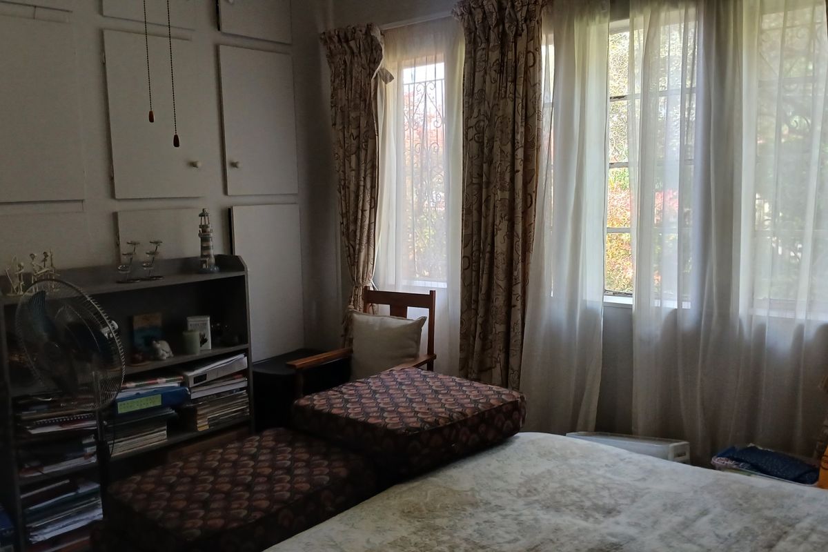 A bedroom featuring built-in cupboards and windows fitted with security bars, offering natural light and functional storage space.