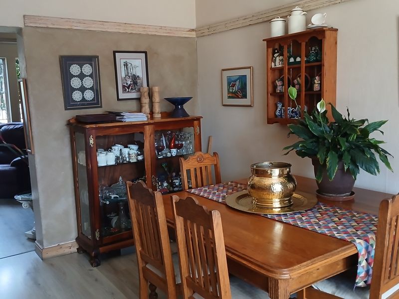 A dining room featuring laminate flooring, a decorative picture rail, and a built-in wall cabinet, with an adjacent view into a secondary living space.