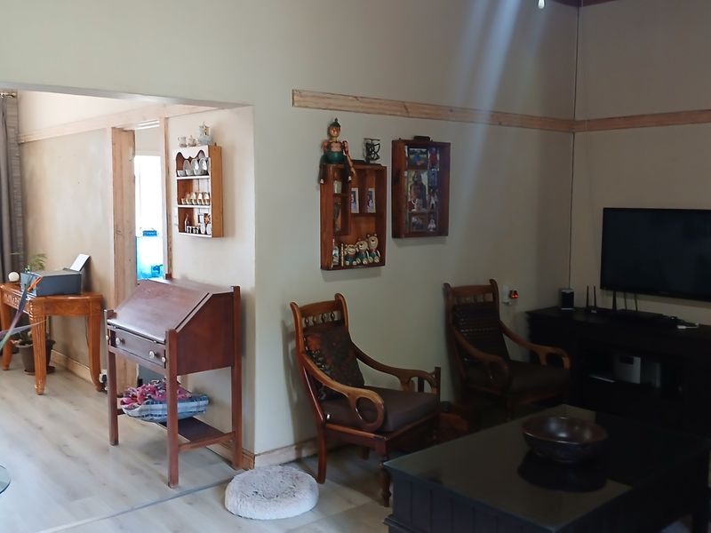 A living room featuring laminate flooring and timber wall trim, with an open archway leading to an adjacent space.