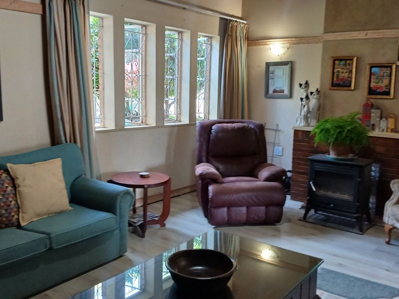 A cozy living room featuring a brick fireplace with a wood-burning stove, laminate flooring, and large windows with security bars.