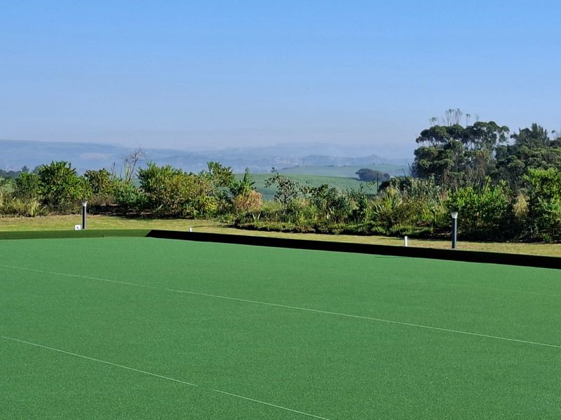 A well-maintained synthetic turf sports facility or bowling green featuring boundary curbing, bollard lighting, and scenic landscape views.
