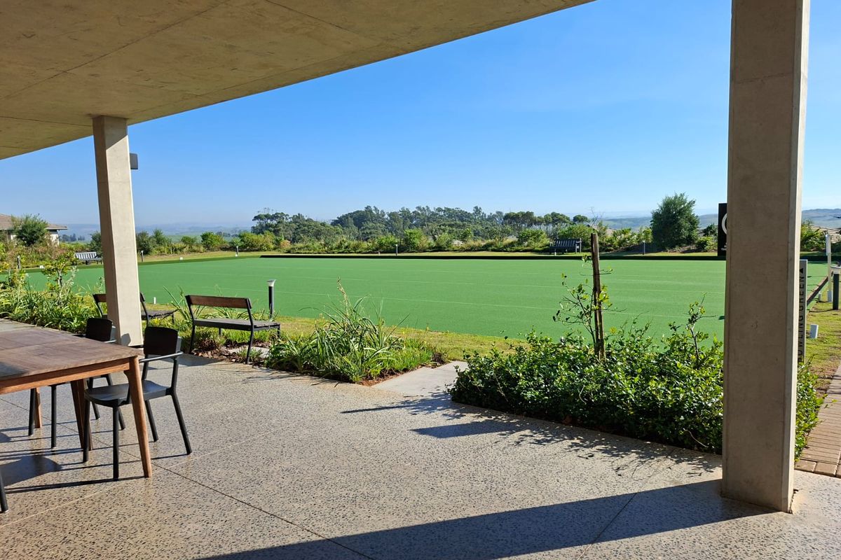 A view from a covered concrete patio overlooking a well-maintained outdoor bowling green in a residential estate setting.
