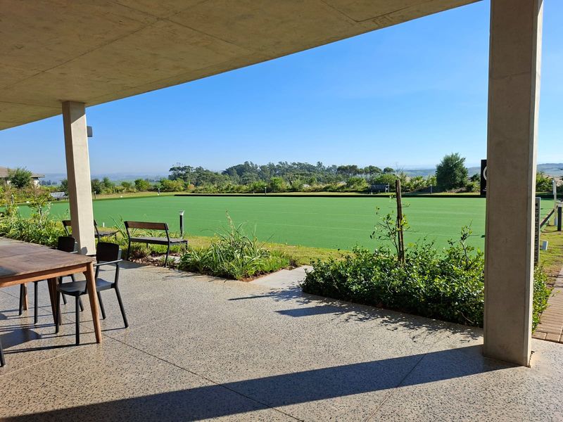 A view from a covered concrete patio overlooking a well-maintained outdoor bowling green in a residential estate setting.