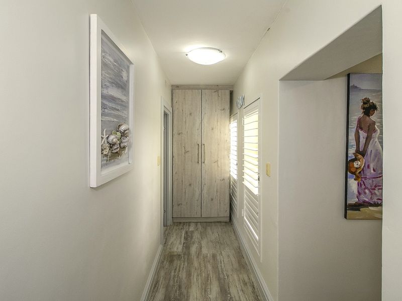 A bright, well-maintained hallway featuring light wood-look laminate flooring, a built-in storage cupboard, and shutter blinds.
