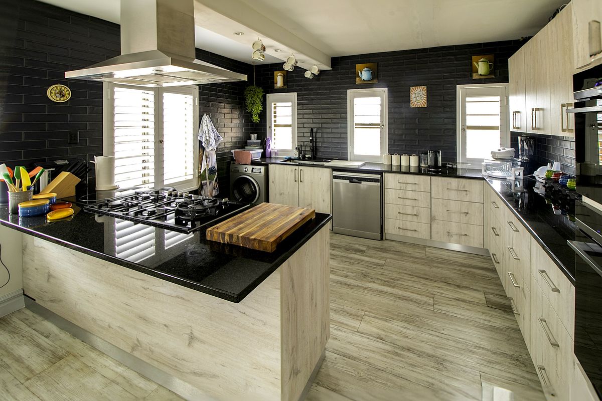 Modern kitchen featuring black granite countertops, wood-look cabinetry, gas cooktop with stainless steel extractor, and stylish black brick-style wall tiling.