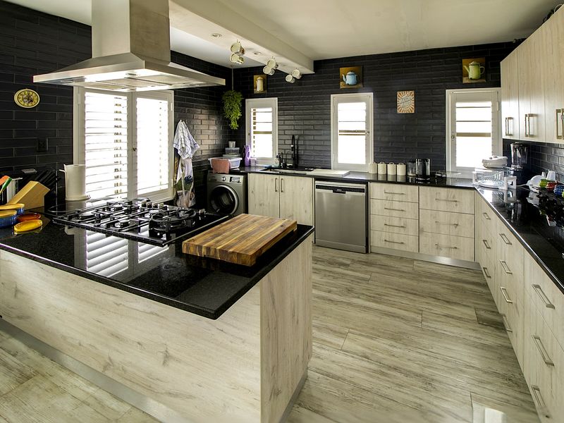Modern kitchen featuring black granite countertops, wood-look cabinetry, gas cooktop with stainless steel extractor, and stylish black brick-style wall tiling.
