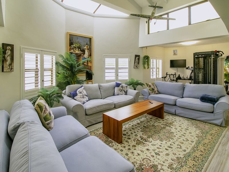 Spacious living room featuring a high vaulted ceiling with skylights, clerestory windows, and plantation shutters, creating a bright and airy atmosphere.