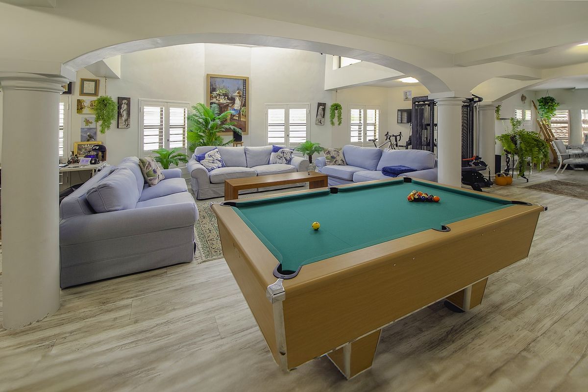 Spacious open-plan living area featuring vaulted ceilings, arched architectural columns, and light-toned laminate flooring with abundant natural light through shuttered windows.