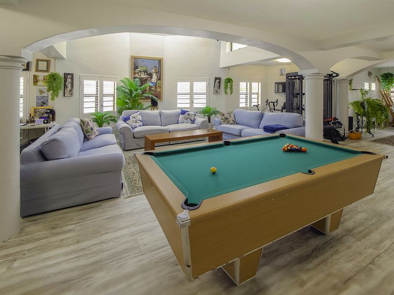 Spacious open-plan living area featuring vaulted ceilings, arched architectural columns, and light-toned laminate flooring with abundant natural light through shuttered windows.