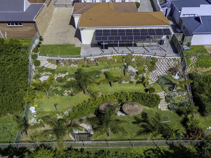 Aerial view of a residential property featuring a large landscaped terraced garden, paved patio area with solar panels, and secure perimeter fencing.