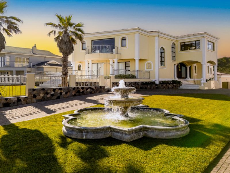 A grand double-story residence featuring a prominent stone fountain, manicured lawn, paved driveway, and elegant architectural columns at the front entrance.