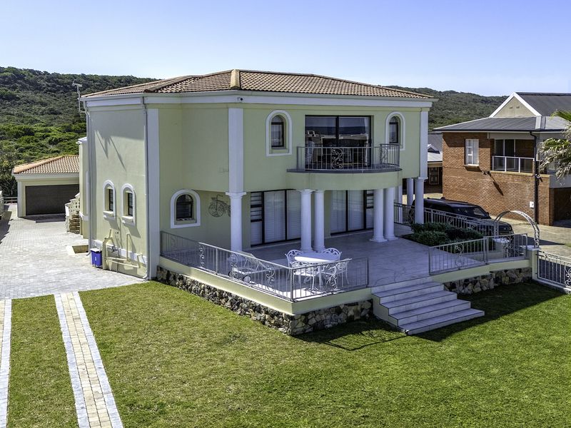 A two-story residential property featuring a rear paved patio, balcony with metal railings, stone cladding accents, and a well-maintained lawn.