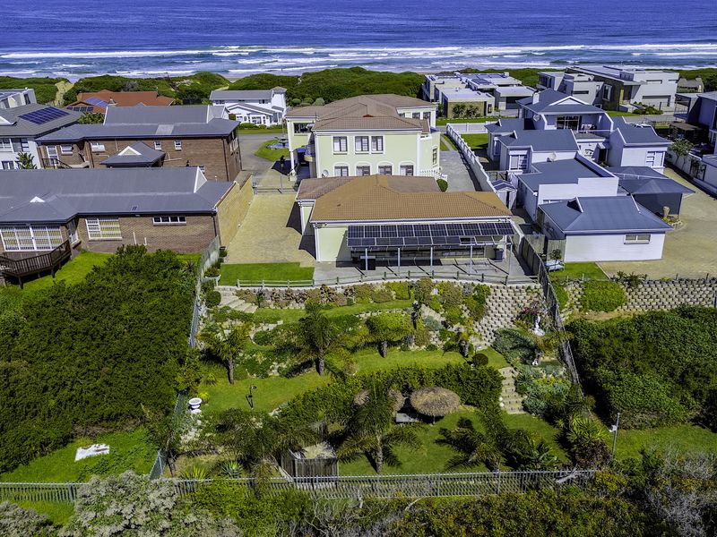 Aerial view of a coastal property featuring a landscaped rear garden, paved patio area, and solar panel installation on the roof.