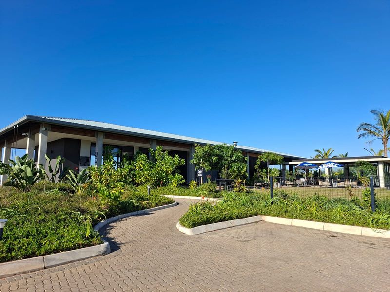 A well-maintained modern building exterior featuring a paved driveway, landscaped garden, and a spacious covered patio area under a metal roof.