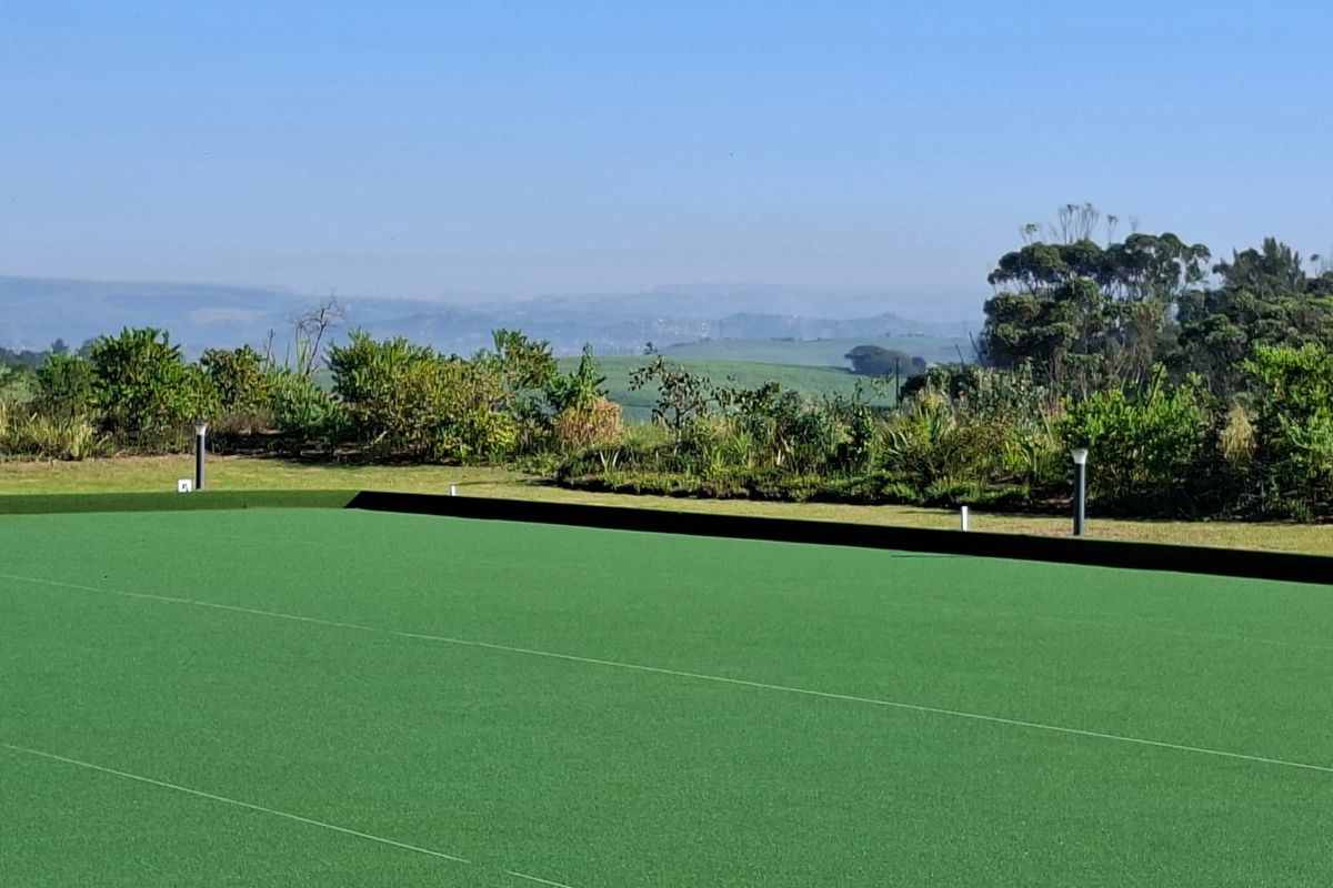 A well-maintained synthetic turf sports facility or bowling green featuring boundary curbing, bollard lighting, and scenic landscape views.