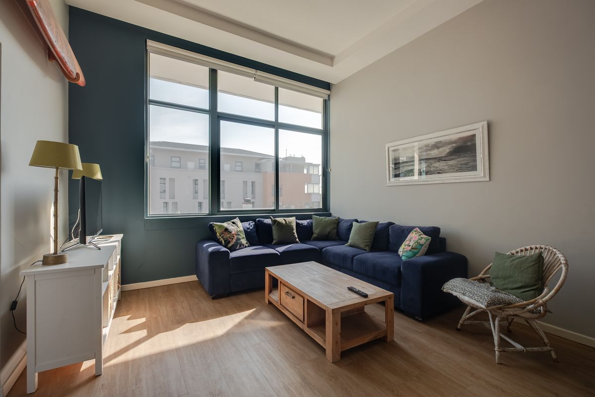 A bright living room featuring large windows, laminate flooring, and a modern recessed ceiling detail, offering a comfortable and well-lit space.