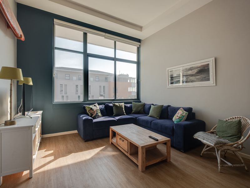 A bright living room featuring large windows, laminate flooring, and a modern recessed ceiling detail, offering a comfortable and well-lit space.