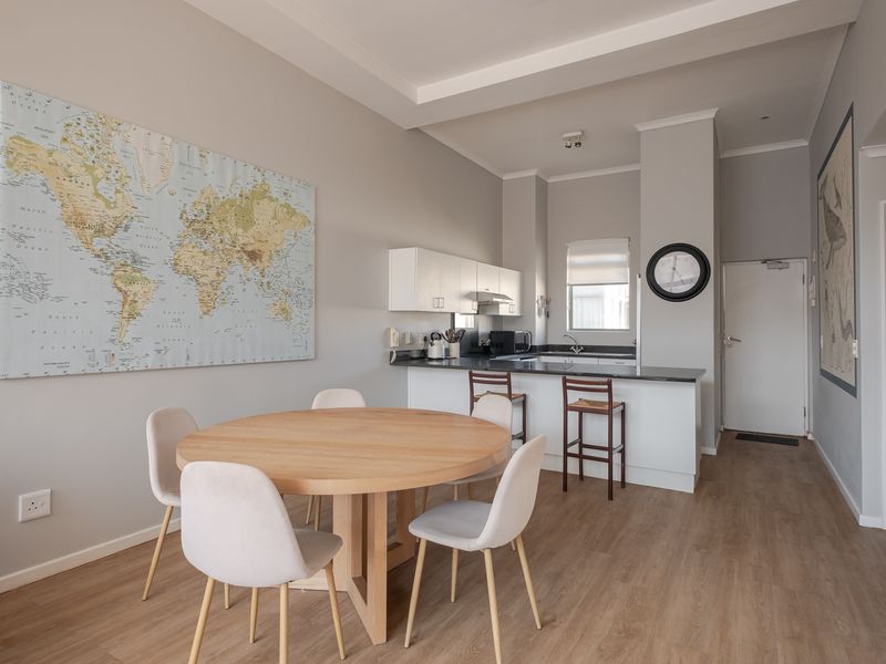 An open-plan living and dining area featuring a modern kitchen with stone countertops, laminate flooring, and a clean, neutral aesthetic.