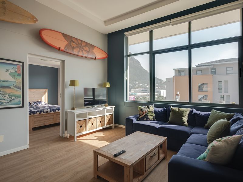 A bright and modern living room featuring large windows with mountain views, laminate flooring, and a seamless transition into the adjacent bedroom.