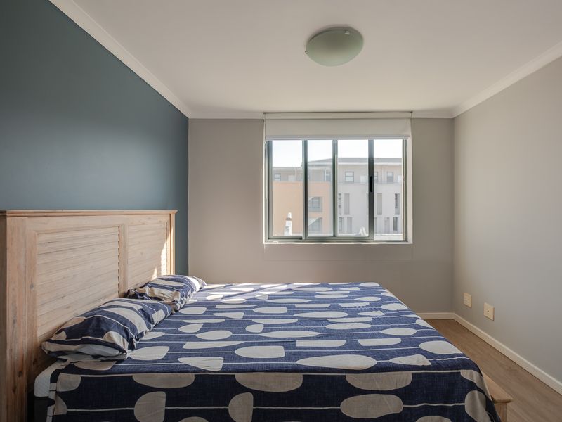 A well-maintained bedroom featuring laminate flooring, a feature wall, and an aluminium-framed window with a roller blind.