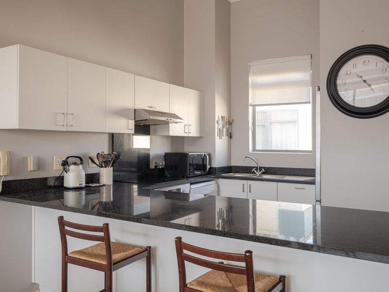 Modern kitchen featuring sleek white cabinetry, contrasting black granite countertops, integrated extractor fan, and a functional breakfast bar area.