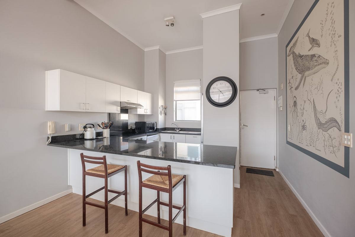 A functional kitchen featuring granite countertops, white cabinetry, and laminate flooring, designed with a breakfast bar for casual dining.