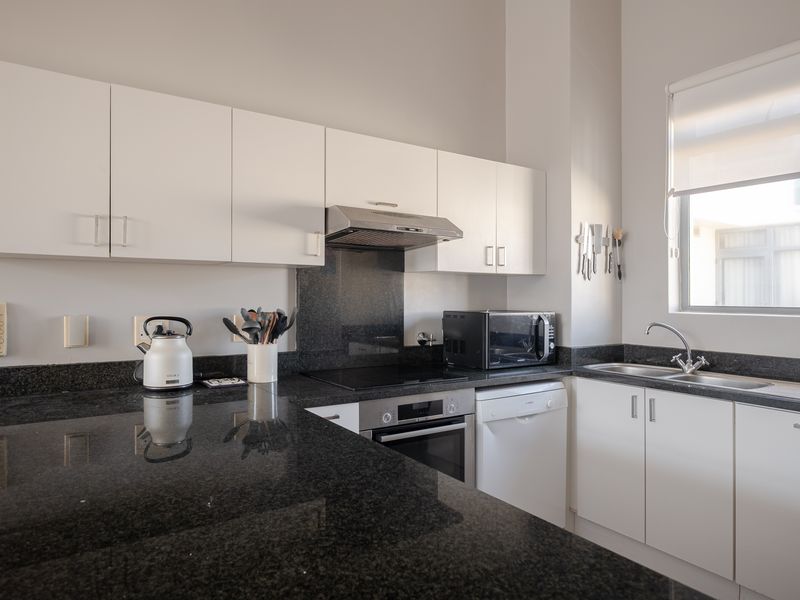 A well-maintained kitchen featuring white cabinetry, dark granite countertops, a built-in oven, electric hob, and a stainless steel sink with a window view.