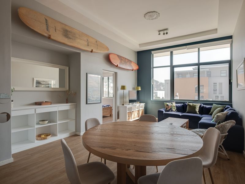 Bright open-plan living and dining area featuring laminate flooring, built-in shelving, and large windows with natural light.