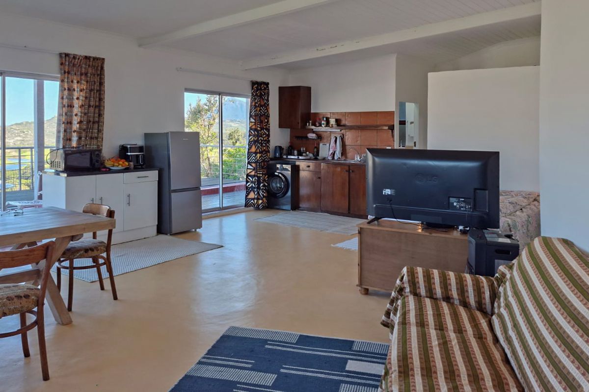 Open-plan living area featuring a kitchenette with built-in cabinetry, tiled backsplash, and sliding glass doors leading to an outdoor space with scenic views.