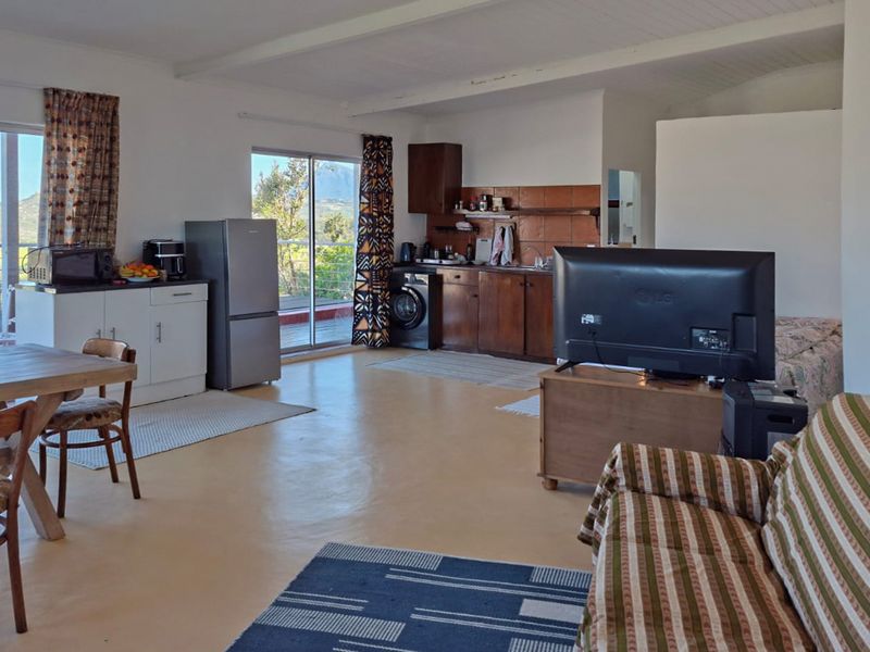 Open-plan living area featuring a kitchenette with built-in cabinetry, tiled backsplash, and sliding glass doors leading to an outdoor space with scenic views.