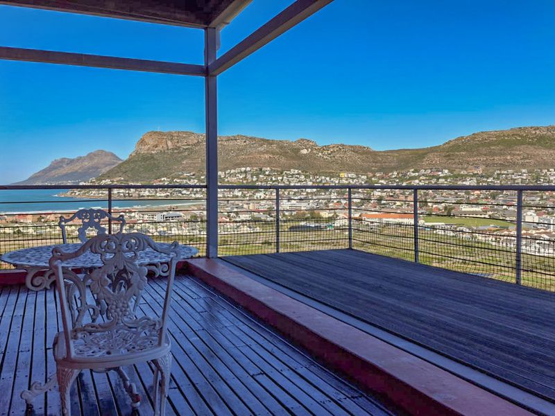 Spacious elevated balcony featuring timber decking and metal railings, offering expansive panoramic views of the coastal town and surrounding mountains.