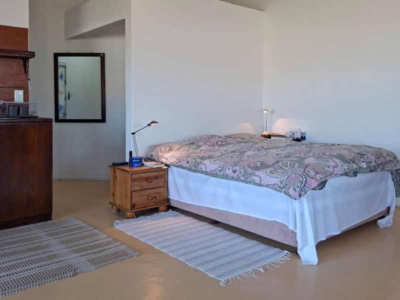 Open-plan studio space featuring a compact kitchenette with built-in cabinetry, sink, and tiled splashback, integrated with a bedroom area.
