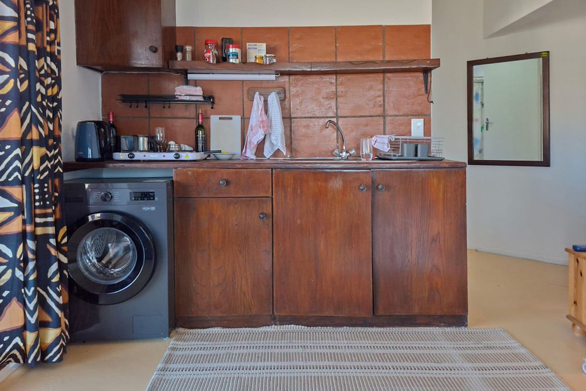 A compact kitchen area featuring dark wood cabinetry, a terracotta tile backsplash, and a stainless steel sink, presenting a dated aesthetic.