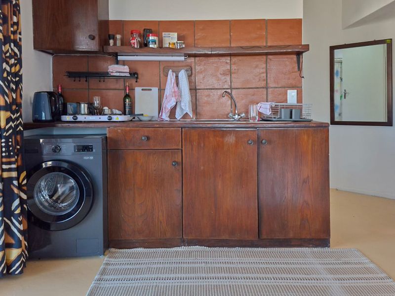 A compact kitchen area featuring dark wood cabinetry, a terracotta tile backsplash, and a stainless steel sink, presenting a dated aesthetic.
