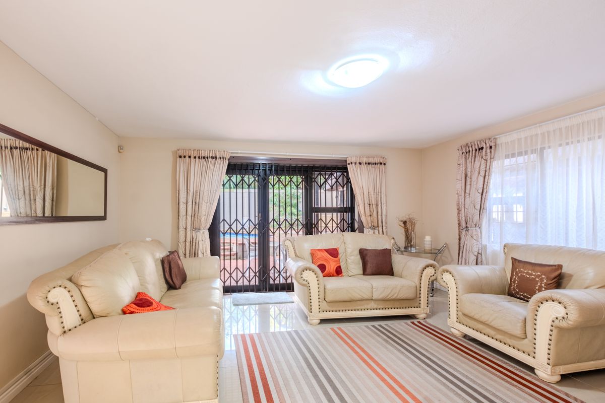 A bright living room featuring tiled flooring, a central ceiling light, and a sliding glass door with a security gate leading to the patio.