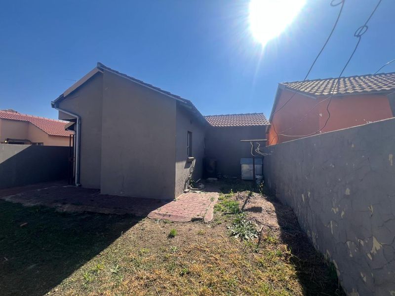 Rear exterior view of the property featuring a tiled roof, paved walkway, and boundary wall with visible maintenance requirements.