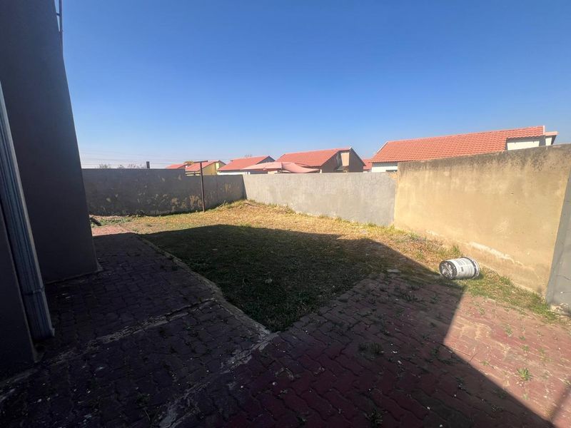 A rear garden area featuring a paved patio, lawn, and perimeter boundary walls, offering potential for landscaping and outdoor living improvements.