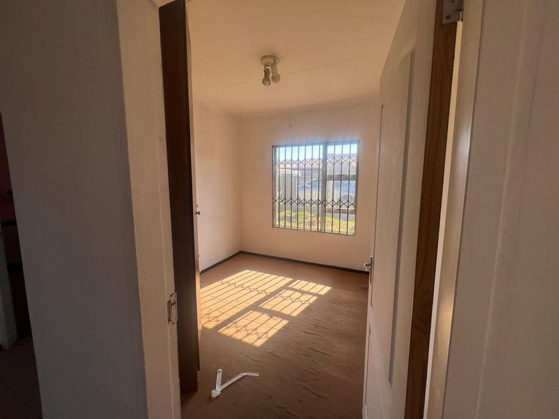An empty bedroom featuring carpet flooring and a window fitted with security bars, offering a blank canvas for renovation.