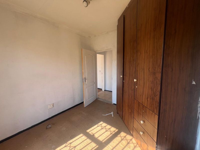 An empty bedroom featuring built-in wooden cupboards, carpeted flooring, and a standard internal door, offering a blank canvas for renovation.