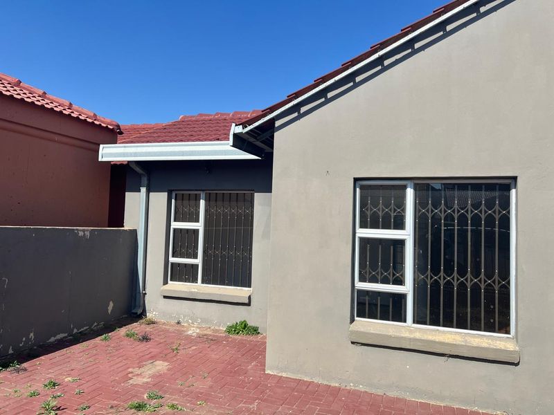 Rear exterior view of the property featuring a paved patio area, tiled roof, and security gates on the windows.
