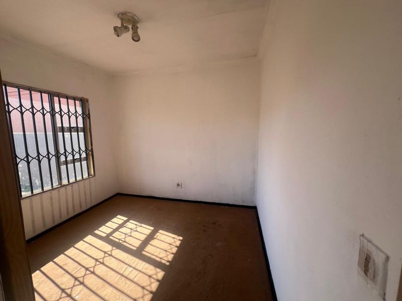 An empty bedroom featuring a security gate on the window, carpeted flooring, and a standard ceiling light fixture.