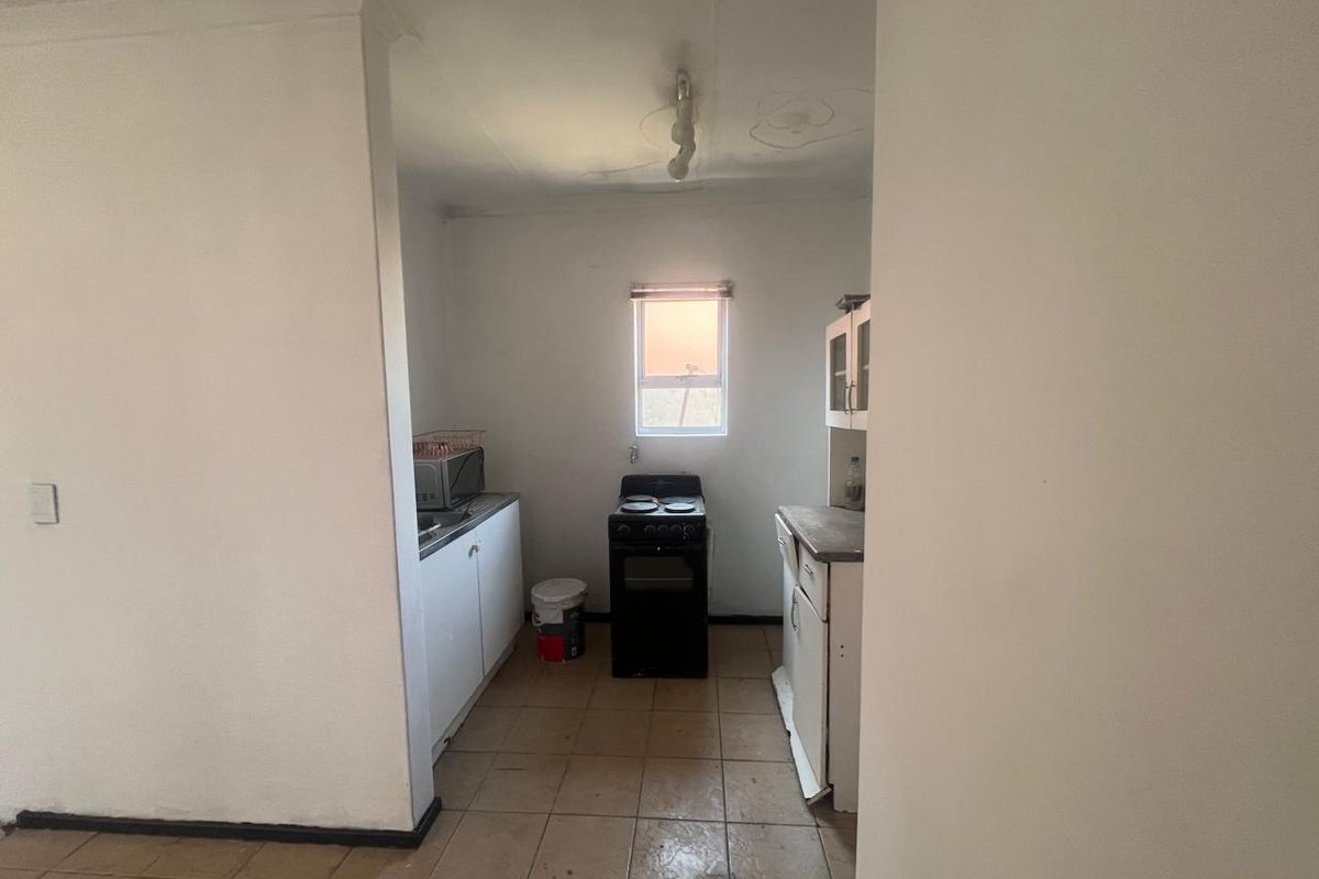 A compact kitchen featuring basic cabinetry, a freestanding stove, and tiled flooring, requiring cosmetic updates and ceiling repairs.