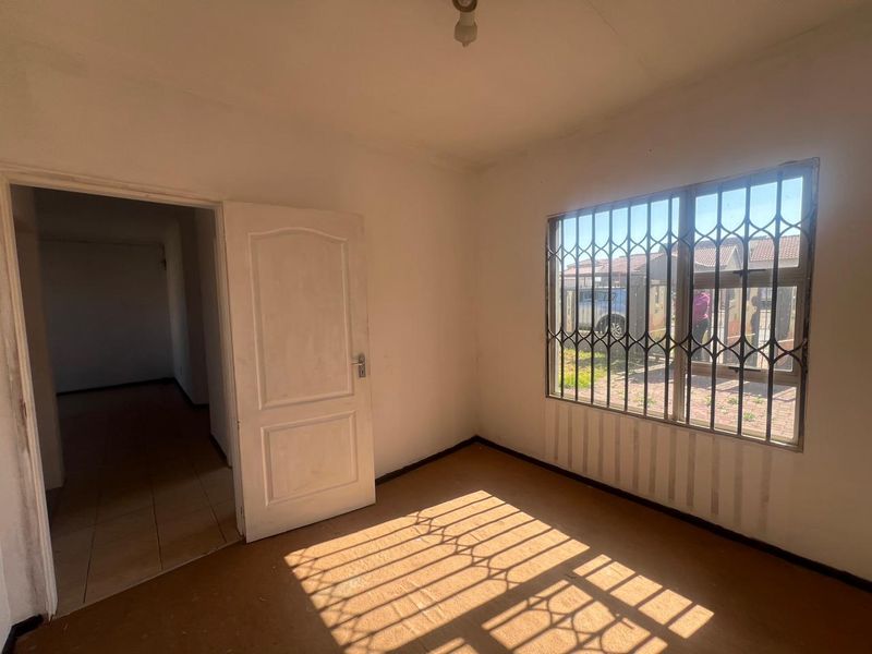 An empty bedroom featuring a window with security bars and an internal door, offering a blank canvas for renovation.