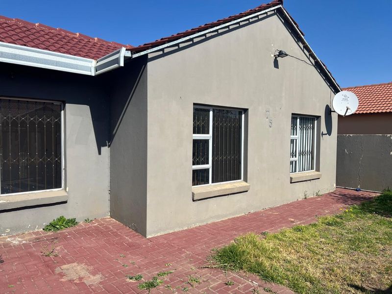 Front exterior view of the house featuring a tiled roof, aluminium window frames with security bars, and a brick paved walkway.