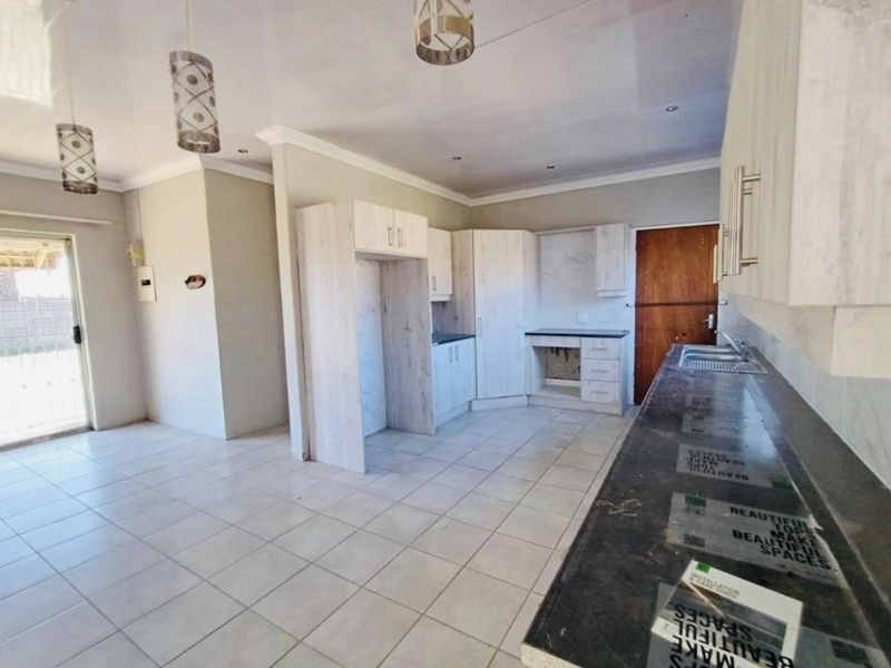 A bright, empty kitchen featuring light-toned built-in cabinetry, dark laminate countertops, tiled flooring, and modern pendant lighting fixtures.