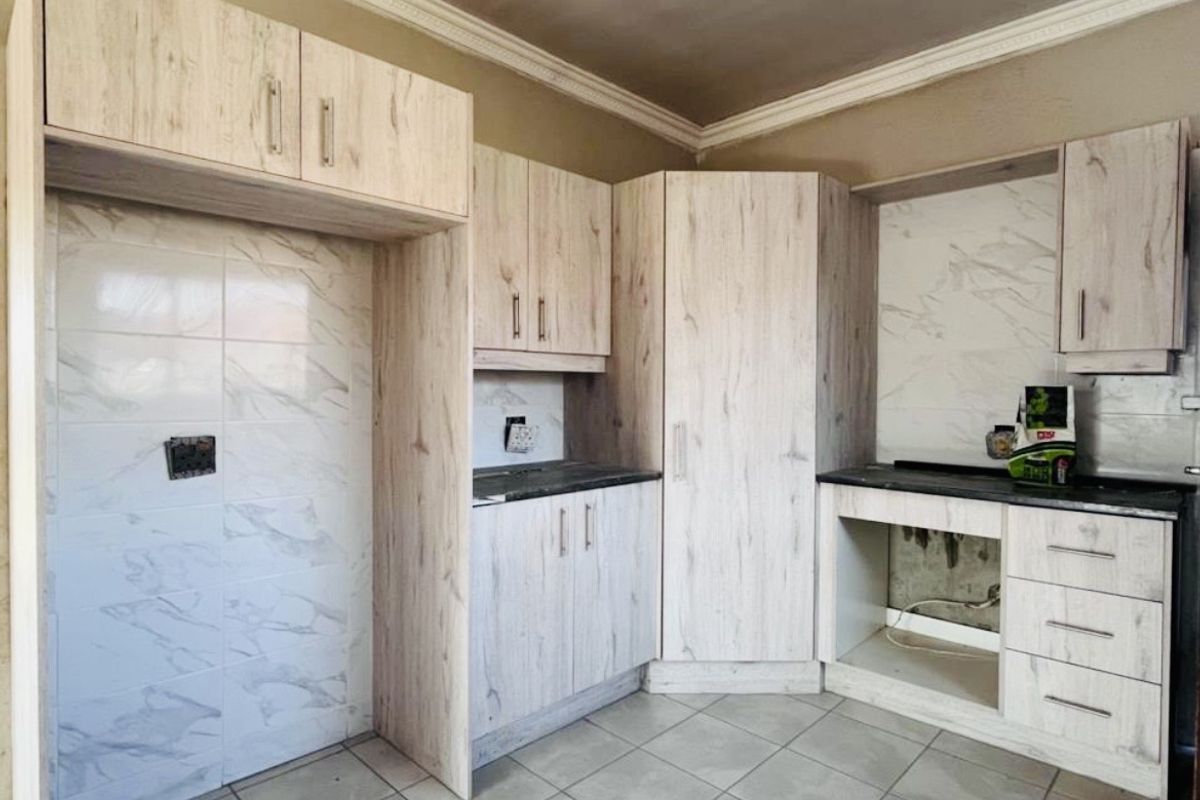 A kitchen featuring light wood-look cabinetry, stone-effect tiled splashbacks, and ceramic floor tiles, currently awaiting final appliance installation and finishing touches.