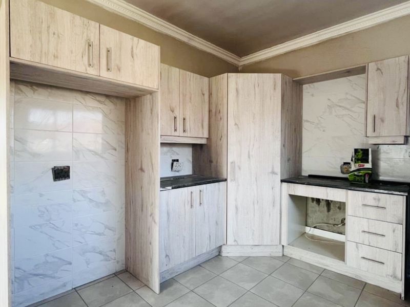 A kitchen featuring light wood-look cabinetry, stone-effect tiled splashbacks, and ceramic floor tiles, currently awaiting final appliance installation and finishing touches.