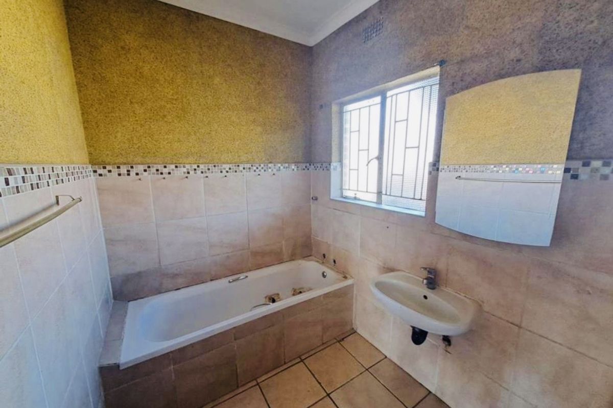 A dated bathroom featuring a built-in bathtub, wall-mounted basin, and tiled finishes, currently requiring maintenance and cosmetic updates to modernize the space.